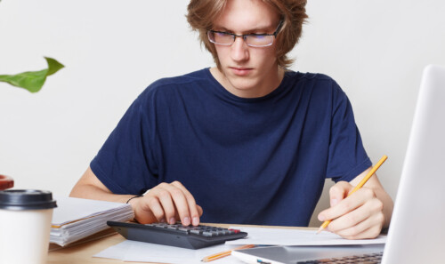 Attractive man faces financial crisis, studies notification from bank, calculates figures. Male student studies math, prepares report, calculates figures. People, business, occupation concept