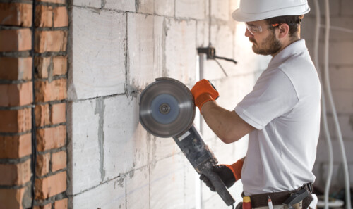 The industrial Builder works with a professional angle grinder to cut bricks and build interior walls. Electrician.