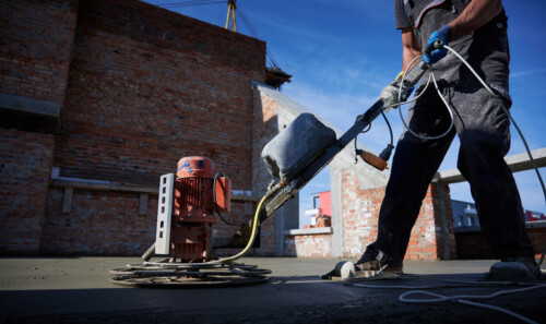 Male worker using concrete screed machine at construction site.
