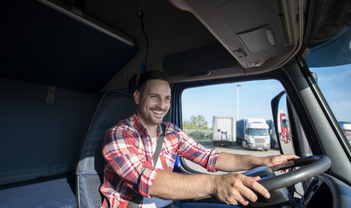 Professional truck driver in casual clothing wearing seat belt on and driving his truck to destination.