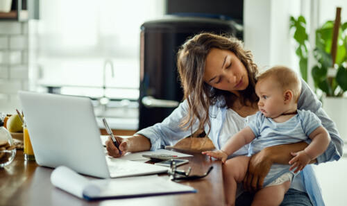 Young mother working on home finances and talking to her baby son.