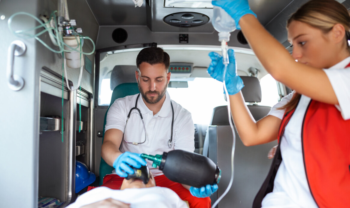 View from inside ambulance of uniformed emergency services workers caring for patient on stretcher during coronavirus pandemic.